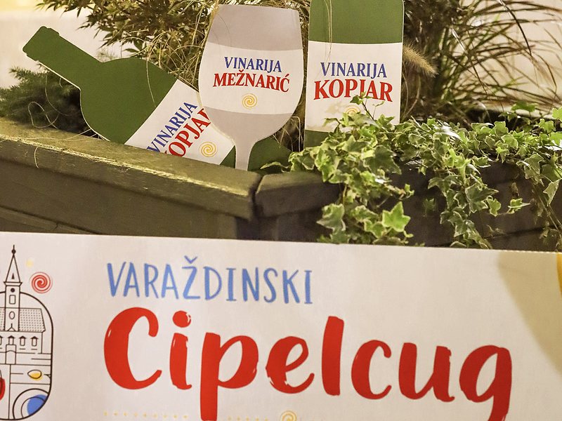Natpis Varaždinskog Cipelcuga s bocama vinarija Kopjar i Mežnarić među zelenilom